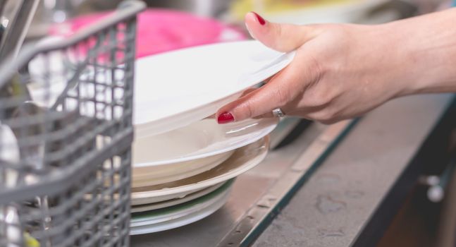 Close-up of a woman's hand filling a dishwasher machine