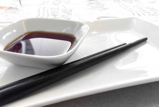 Soy sauce dish with a couple of chopsticks. Shallow depth of field. Defocused blurry background.