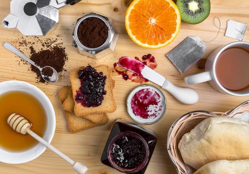 Breakfast table with mug of tea, jam, fresh fruits, bread, rusks and honey. Top view.