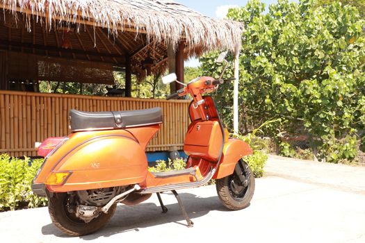 Classic scooter. Orange print Piaggio Vespa parked on a public street in Bali. Vintage scooter wheel and body design details. Indonesia, June 2019.