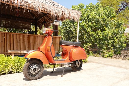Classic scooter. Orange print Piaggio Vespa parked on a public street in Bali. Vintage scooter wheel and body design details. Indonesia, June 2019.