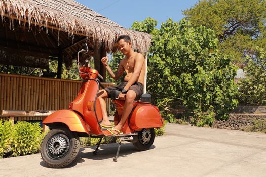 Bali, Indonesia, 1th of July, 2019. Youg Indonesia man is sitting on orange Classic Vespa. Orange Classic Vespa. A old orange Vespa Super motorscooter is parked on a sidewalk.