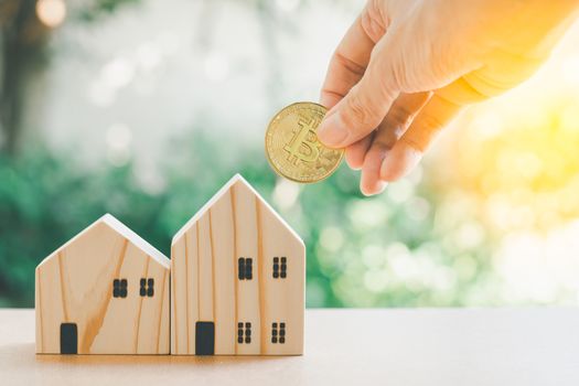 Saving money concept. Hand hold gloden coin with wooden model home on table with green bokeh background. Saving or investment for home in the future.