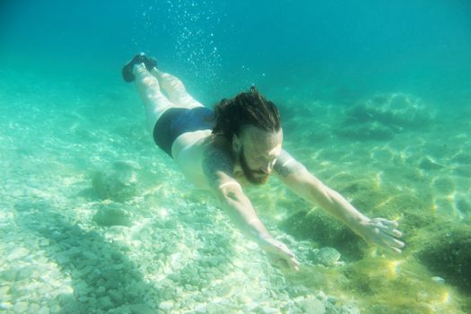 Mid adult bearded long hair man swimming underwater in mediterranean adriatic sea in Croatia