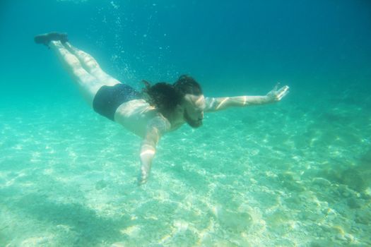 Mid adult bearded long hair man swimming underwater in mediterranean adriatic sea in Croatia