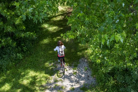 A girl with a backpack rides a red bike along a path among the trees