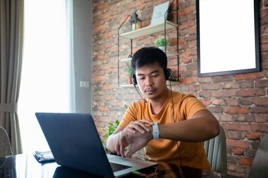 Asian man is watching the time and he uses a notebook computer to work at home.