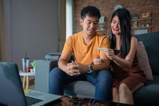 Happy Asian couple smiling looking cheerful after a home pregnancy test in sofa at home