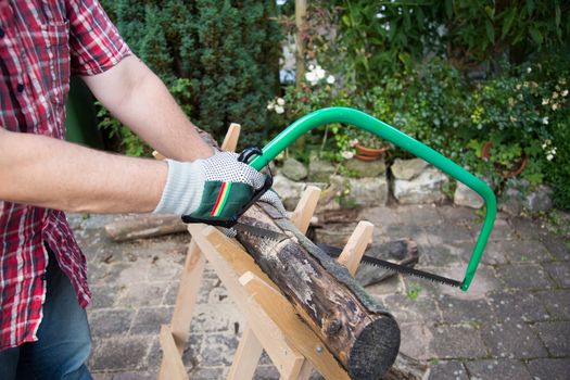 Sawing firewood manually with a hacksaw on a wooden sawhorse