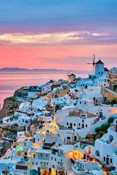 Famous greek iconic selfie spot tourist destination Oia village with traditional white houses and windmills in Santorini island on sunset in twilight, Greece