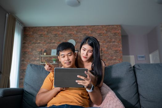 Asian Couple shopping online and paying with credit card at laptop computer,Happy couple at home surfing the net on sofa