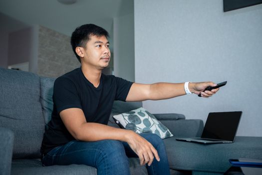 Asian man is watching football on tv and sit on the sofa at home on a holiday and smiling and laughing happy