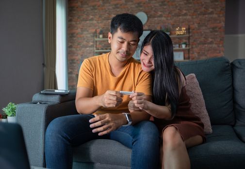 Happy Asian couple smiling looking cheerful after a home pregnancy test in sofa at home