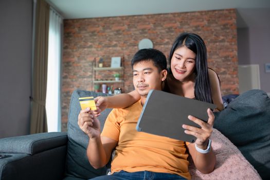 Asian Couple shopping online and paying with credit card at laptop computer,Happy couple at home surfing the net on sofa