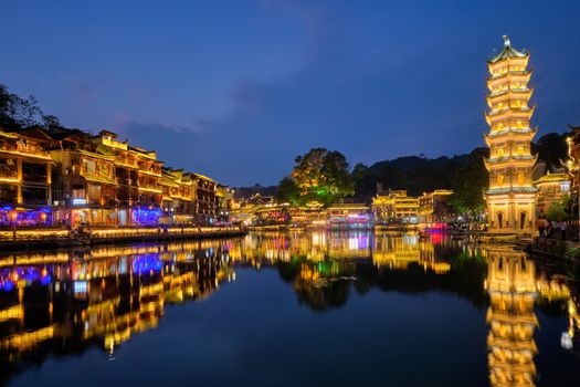 Chinese tourist attraction destination - Feng Huang Ancient Town (Phoenix Ancient Town) on Tuo Jiang River with Wanming Pagoda illuminated at night. Hunan Province, China