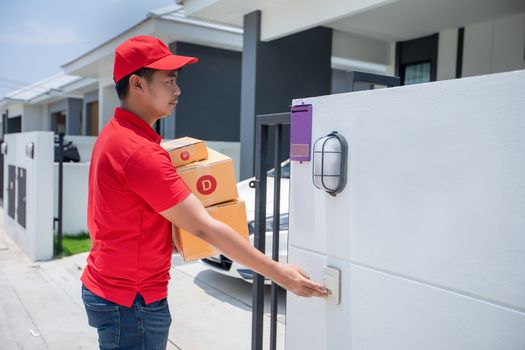 Asian delivery servicemen wearing a red uniform with a red cap handling cardboard boxes to give to the customer in front of the house and Click the doorbell. Online shopping and Express delivery