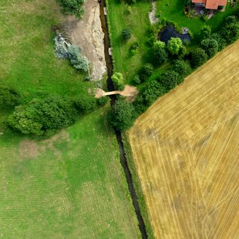 Aerial photograph of farmland and meadows crossed by a small tamed brook, abstract aerial view, made with drone