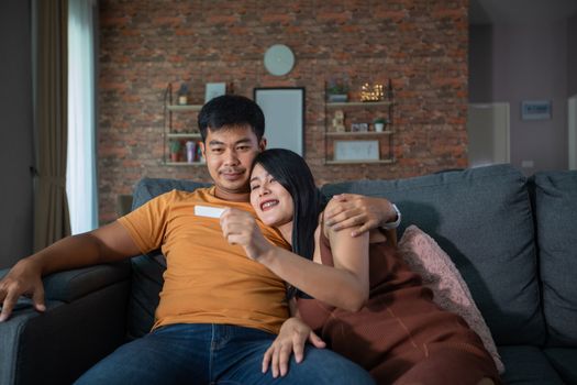 Happy Asian couple smiling looking cheerful after a home pregnancy test in sofa at home