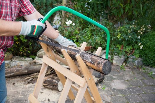 Sawing firewood manually with a hacksaw on a wooden sawhorse