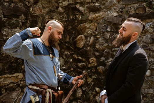 A man in Viking clothes challenges his alter ego who derides him in contemporary clothes, the same man face to face in clothes from different eras
