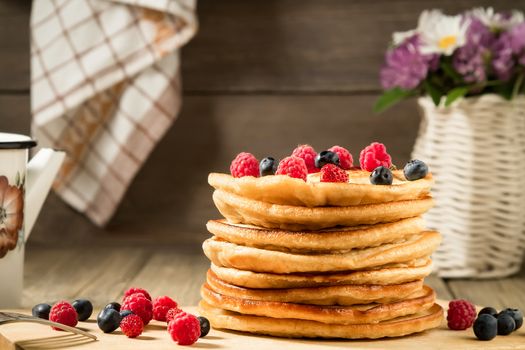 Stack of pancakes with berries on a wooden table in a rustic style.