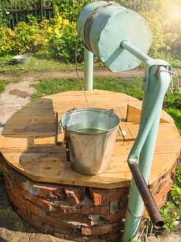 Metal bucket on a wooden lid of a brick well, open on a Sunny summer day.