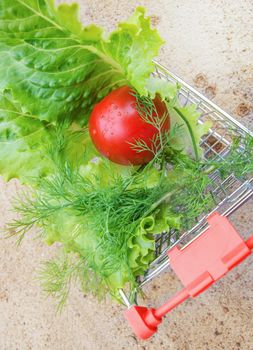 Basket full of various fresh vegetables tomato, lettuce, dill, sand background, top view.