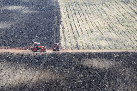 Two tractors working on burned farmland.