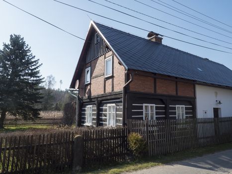 View from road on old rustic cottage half timbered house in small village Marenicky in luzicke hory, Lusatian Mountains, early spring, blue sky.