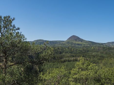 Spring landscape in Lusatian Mountains with view point hill Klic or Kleis, fresh deciduous and spruce tree forest. Blue sky background, horizontal, copy space.