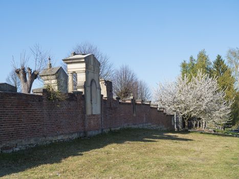 old red brick wall of country cemetery at village Cvikov in luzicke hory, Lusatian Mountains, early spring, blue sky.