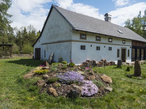 Old half tibered house cootage with garden, rock garden in full bloom with pink Phlox, Armeria maritima, sea thrift, Bergenia or elephants ears, carnation colorful blooming flowers and gazebo pergola.