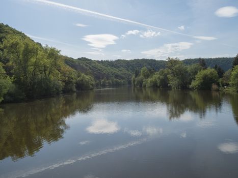 view on river Berounka from pedestrial bridge from village Zadni Treban to Hlasna treban in central Bohemian region, green lush trees reflecting in water, blue sky, spring sunny day,