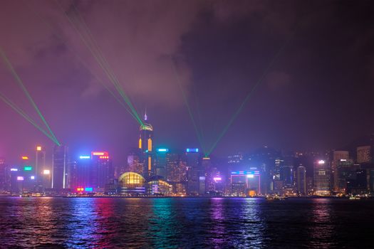 Hong Kong skyline cityscape downtown skyscrapers over Victoria Harbour in the evening illuminated with lasers with tourist boat ferries . Hong Kong, China