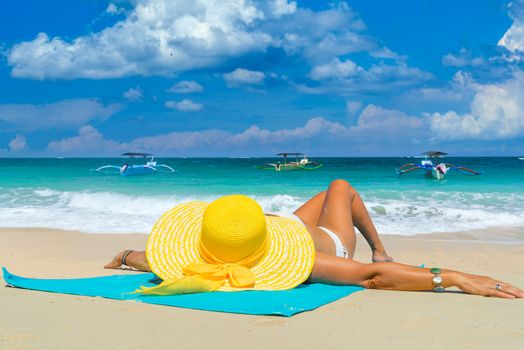 Woman in yellow bikini lying on tropical beach in Bali 