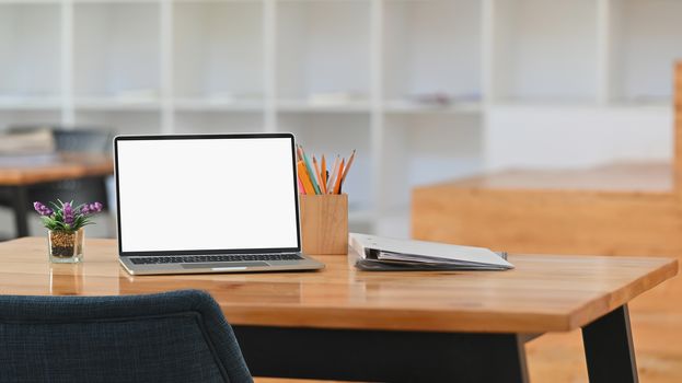 Front of white blank screen laptop, pencil holder, document files, potted plant on a working desk.