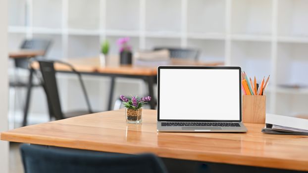 Front view Photo of white blank screen laptop on working desk. Including pencil holder, document files and potted plant on the work desk.