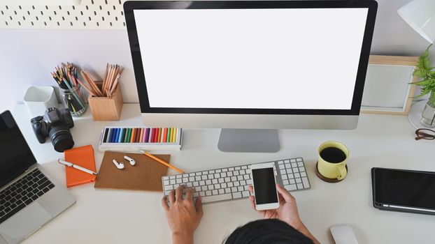 Cropped shot of working desk while businessman are typing and showing mobile in front of white blank screen computer.