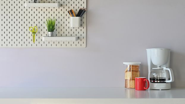 Versatile table in the morning vibe including coffee maker, coffee cup, biscuits is on the table  potted plant, pencil holder and scissors on the white shelf.