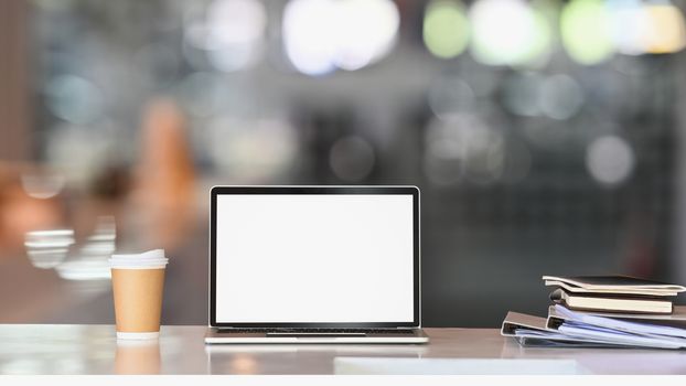 Laptop with white blank screen on white table with coffee cup and document file. Home interior or office background.