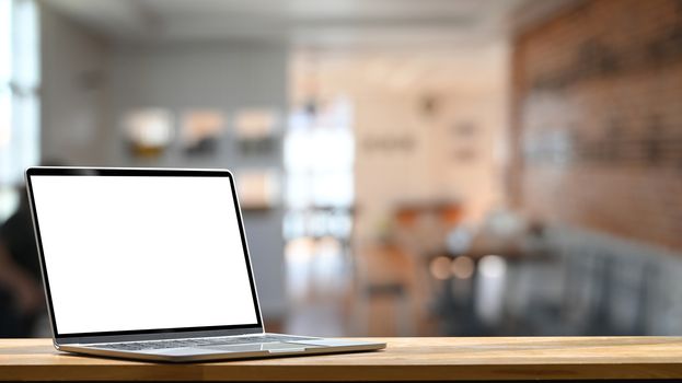 Photo of modern laptop with white blank screen display setting on the wooden table over the blurred modern room.