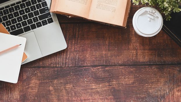 Close-up image of wooden table including book, pencil, coffee cup, potted plant, laptop and notebook.