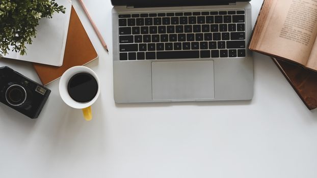 Modern office desk include laptop, camera, coffee cup, notebook, book, potted plant and pencil. Top view of office desk and office equipment.