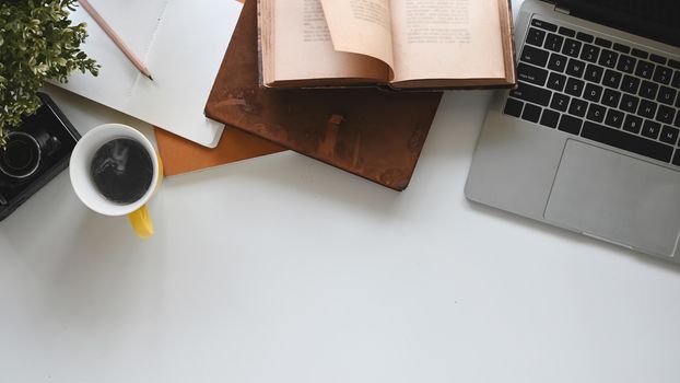Modern office desk include laptop, camera, coffee cup, notebook, book, potted plant and pencil. Top view of office desk and office equipment.