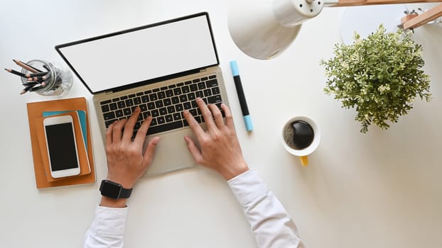 Top view of businessman typing on white blank screen laptop at the modern working desk. Including working equipment on desk.