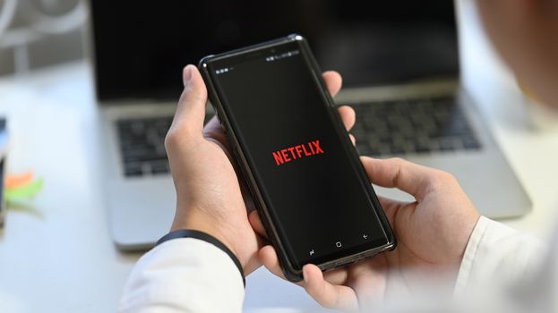 CHIANGMAI, THAILAND JAN 25 2020 : opening Netflix application icon on Samsung Note 9 man resting with his cell phone in his hands and the Netflix logo in the screen.