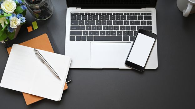 Top view office equipment such as laptop, white blank smartphone, notebook, pen, coffee cup and potted plant putting on modern working desk. Comfortable modern working desk concept.