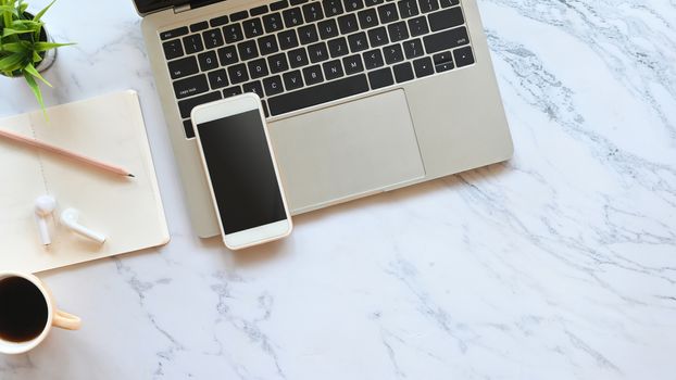 Laptop, black blank screen smartphone, wireless earphone, pencil, notes and potted plant putting on the marble table. Flat lay working equipment concept.