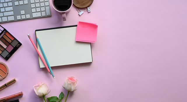 Top view image of feminine working desk including coffee cup, modern keyboard, notebook, pencil, bouquet and cosmetics putting on it. Women's working desk concept.