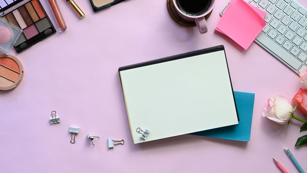 Top view image of feminine working desk including coffee cup, modern keyboard, notebook, pencil, bouquet and cosmetics putting on it. Women's working desk concept.